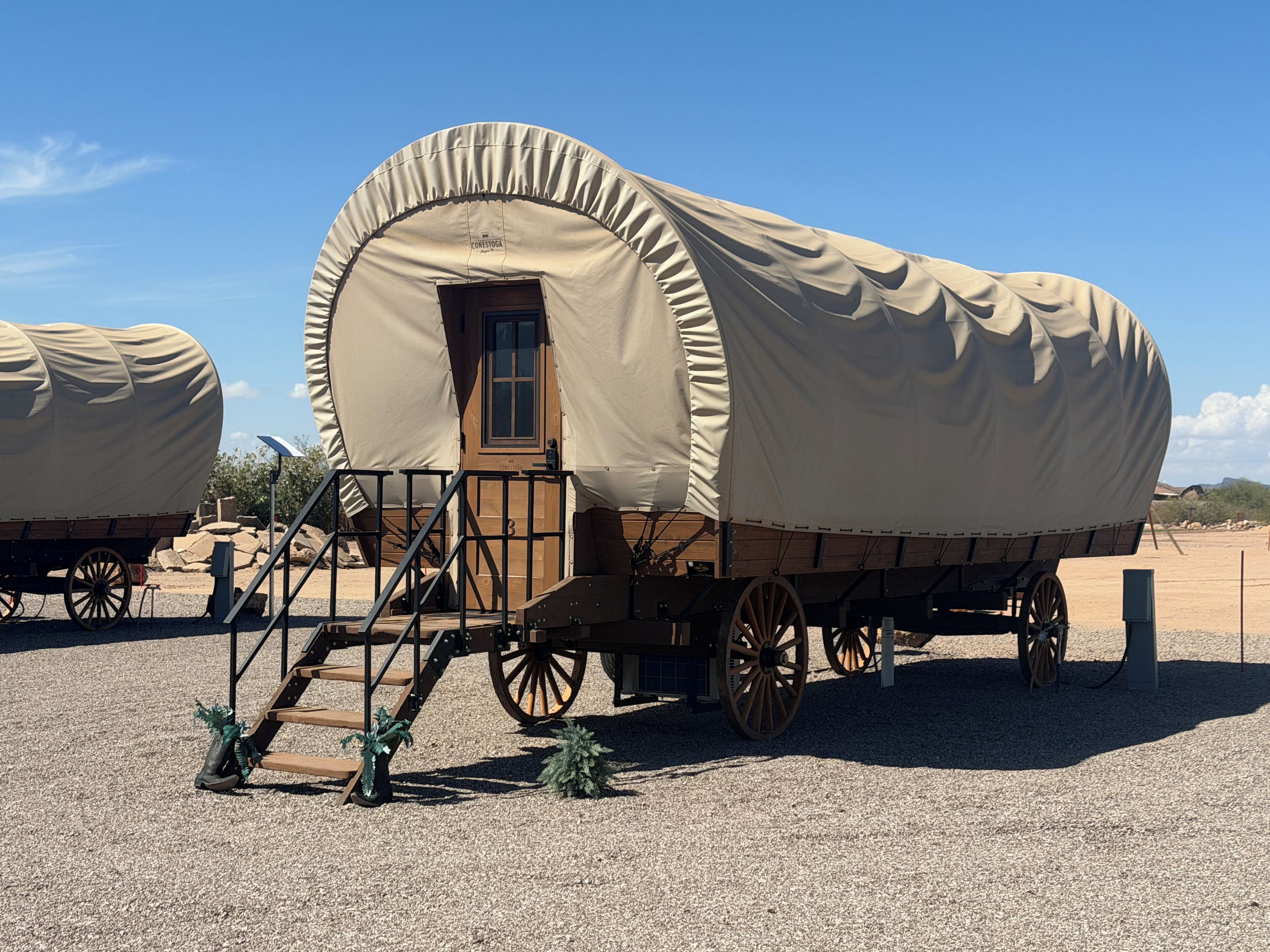 A covered wagon with a wooden door and steps leading up to it, parked on a gravel surface.