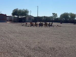 Un espace recouvert de gravier, avec des chaises Adirondack disposées en cercle, entouré de rochers et de quelques arbres.