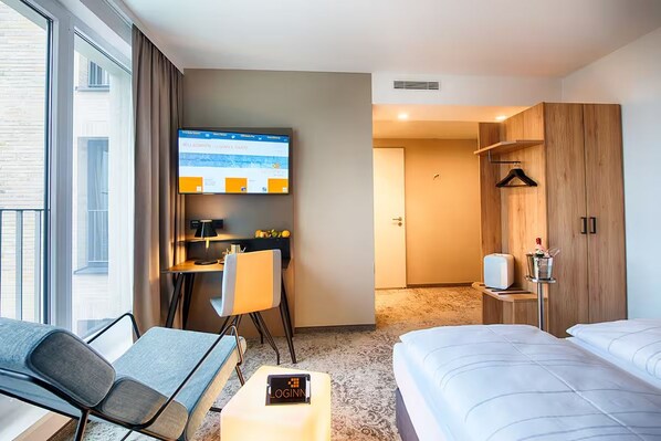 Ein Hotelzimmer mit einem Bett, einem Schreibtisch mit Computer, einem Fernseher und Blick ins Freie.