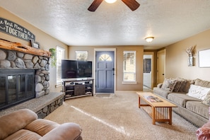 A living room with a stone fireplace, a television, a sofa, and a coffee table. - The Otter House - Tumalo Steps To River, Fire Pit, Games (Bend)