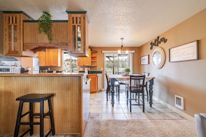 Een keuken met houten kasten, een bar en een eettafel met stoelen.