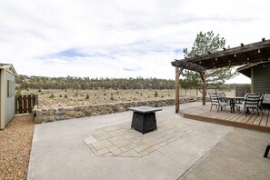 Ein Außenbereich mit einer Steinterrasse, einem Tisch und Stühlen, einer Pergola mit Lichterketten und Blick auf einen bewaldeten Hügel.