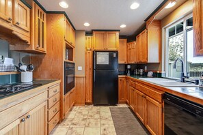 A kitchen with wooden cabinets, a black refrigerator, a stove, and a dishwasher. - The Otter House - Tumalo Steps To River, Fire Pit, Games (Bend)