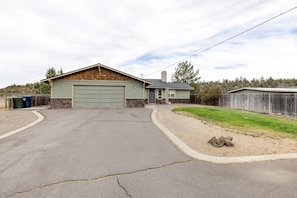 A single-story house with a garage, a front yard with a lawn, and a wooden fence. - The Otter House - Tumalo Steps To River, Fire Pit, Games (Bend)