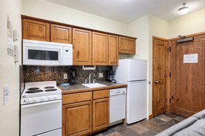A compact kitchen with wooden cabinets, a microwave, a stove, a sink, and a refrigerator. - Studio on Snowflake unit 204 (Breckenridge)