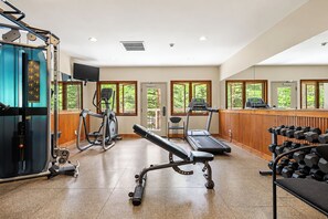 Et fitnessrum med træningsudstyr, en bænk og et tv ophængt på væggen.
