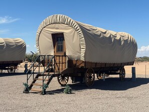 A covered wagon with a wooden door and steps leading up to it, parked on a gravel surface. - WG #6-bedroom recreational vehicle with AC in nice Casa Grande (Casa Grande)