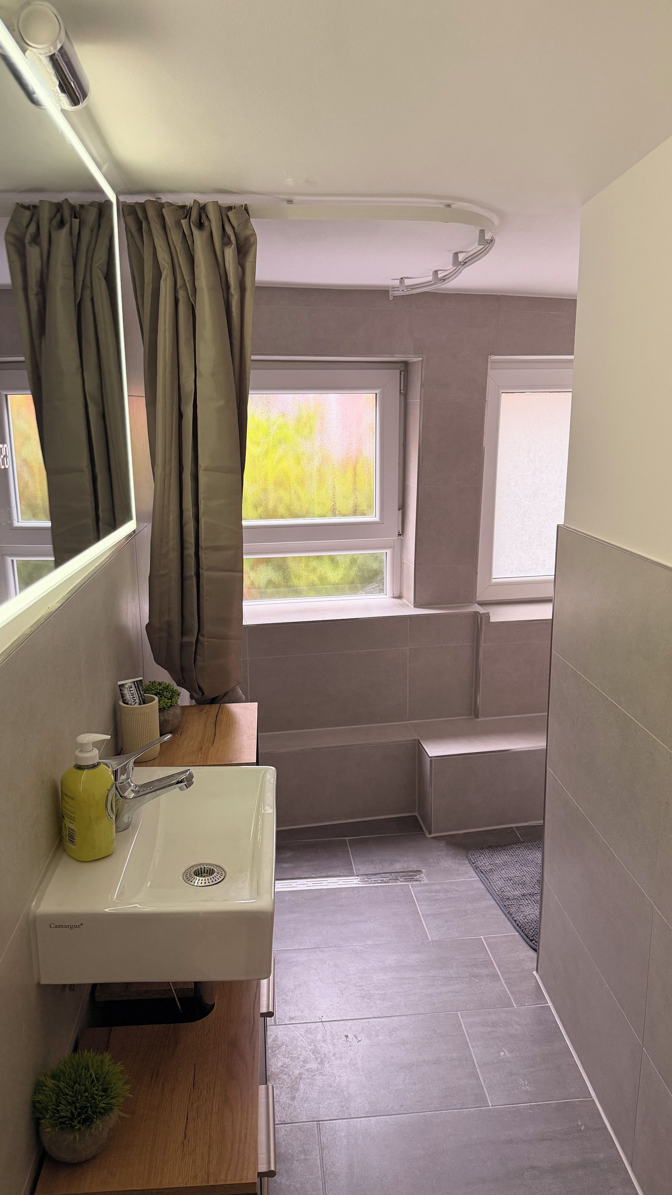 Ein Badezimmer mit Waschbecken, Spiegel, Dusche und zwei Fenstern.