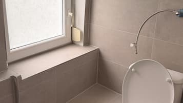 A bathroom with a toilet, a window, and a shower.
