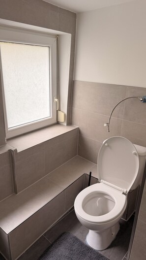 A bathroom with a toilet, a window, and a shower. - New Listing (Reutlingen)