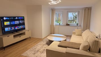 A modern living room with a flat-screen TV, a sofa, a coffee table, and a window with curtains.