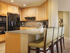 A kitchen with wooden cabinets, a stainless steel refrigerator, a granite countertop, and a bar area with chairs. - Luxury 1 Bedroom Getaway at Club Velas Vallarta, All Inclusive Mexico Paradise (Puerto Vallarta)