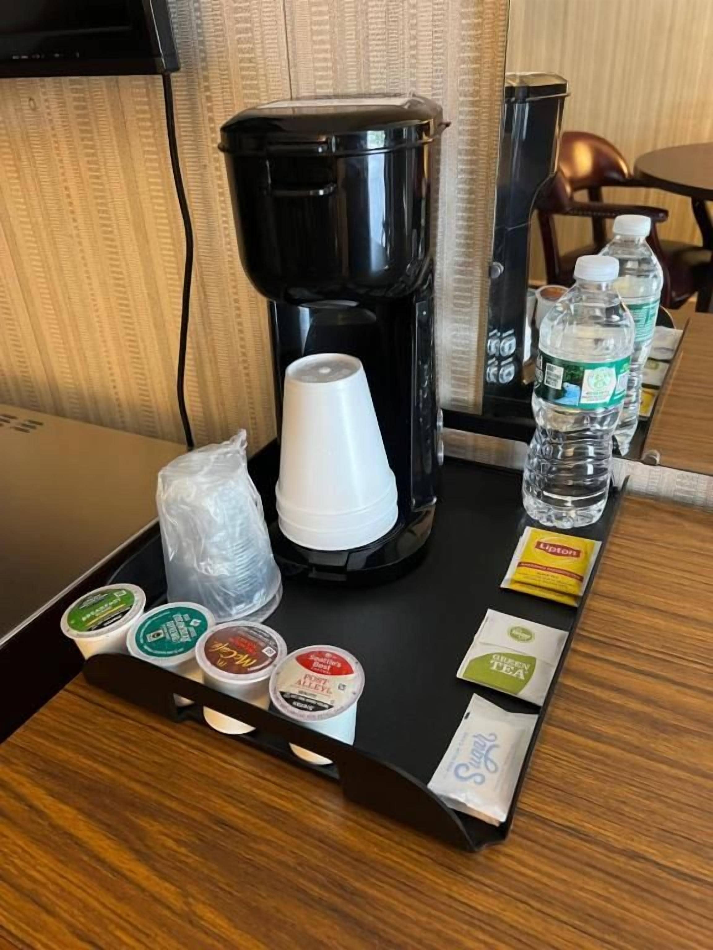Un espace dédié au café, comprenant une machine à café, des gobelets jetables, des bouteilles d’eau et des sachets de thé.