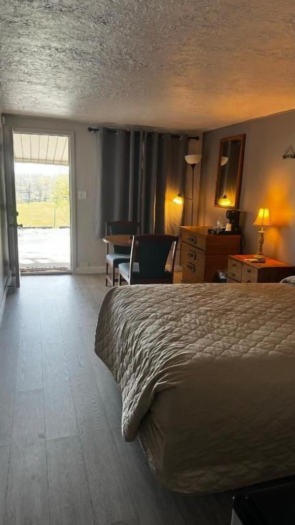 A hotel room with a bed, a desk, a chair, a dresser, and a door leading to a balcony.