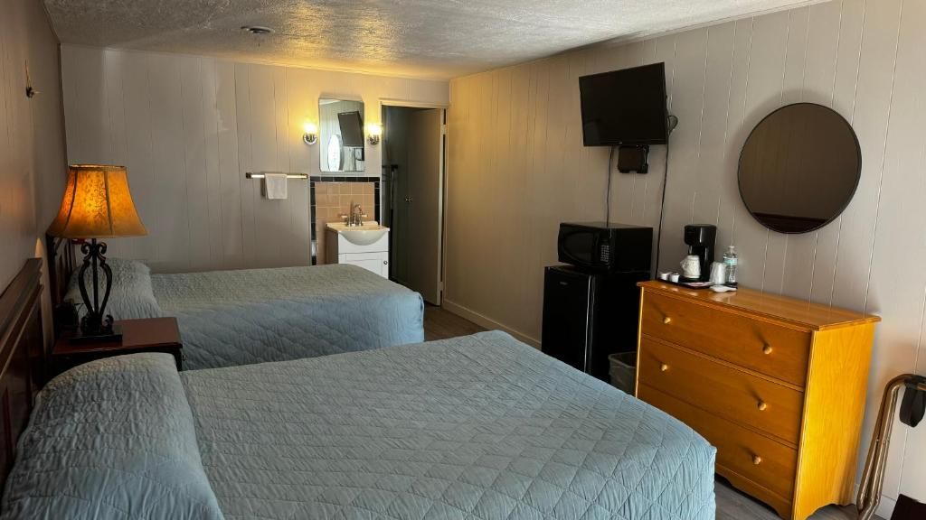 A hotel room with two beds, a wooden dresser, a television, and a bathroom with a sink and mirror.