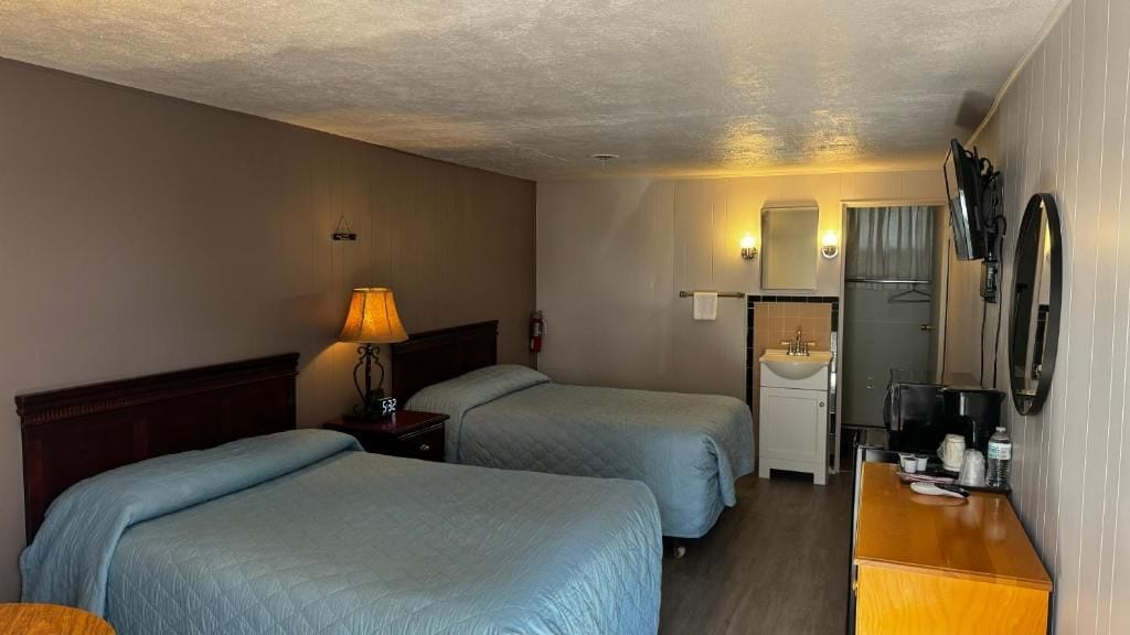 Habitació d'hotel amb dos llits, una taula de nit amb una làmpada, un petit rentapeus, un mirall i una televisió.