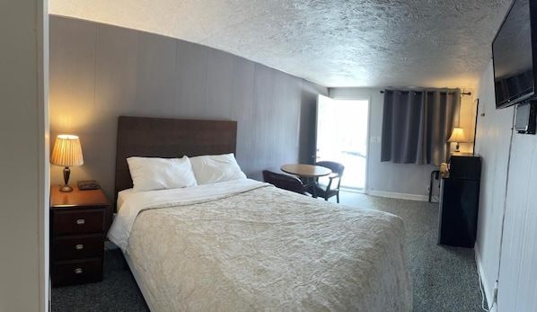 A hotel room with a bed, bedside table, lamp, chair, and a television.