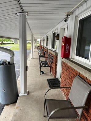 A covered outdoor seating area with chairs and a trash can.