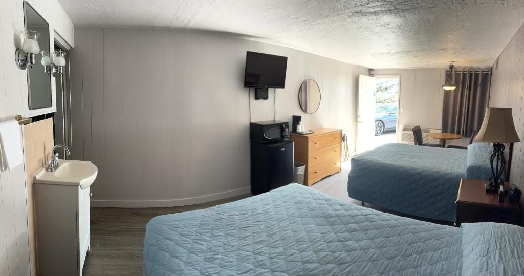 A hotel room with two beds, a sink, a television, and a small table with a lamp.