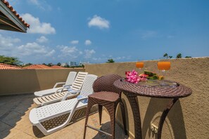 Une terrasse sur le toit, avec des chaises longues, une table où sont servis des boissons et une vue imprenable sur les toits de la ville.