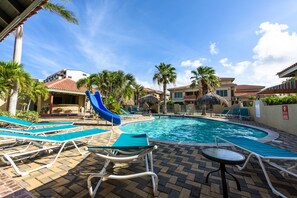 A pool area with lounge chairs, a blue slide, and a clear blue sky. - Palma Real 29 - your vacation Condo in Palm Beach (Palma Real)