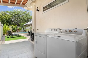 Uma lavanderia com máquina de lavar e secadora, piscina e área de estar coberta com mesa e cadeiras.