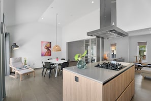 A modern kitchen with a central island, dining area with chairs, and a living space with a sofa and a lamp. - Modern Three Bedroom Villa in Noord (Boegoeroei)