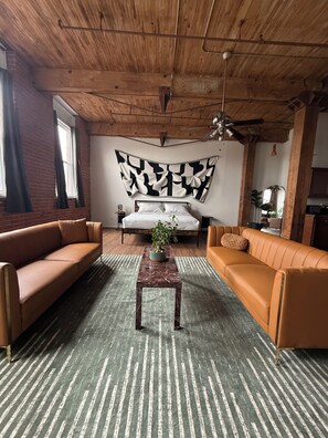 A room with a wooden ceiling, two sofas, a bed, and a large abstract wall hanging. - 420-Friendly King suite Loft Walk to Detroit Riverfront FREE parking (Detroit)