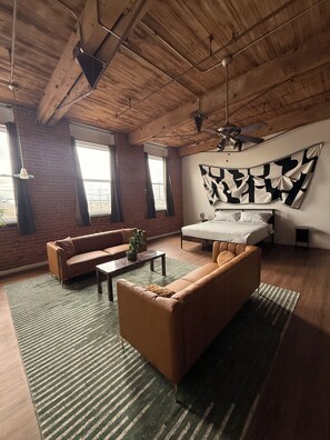A modern living room with a sofa, coffee table, and a large abstract painting on the wall. - 420-Friendly King suite Loft Walk to Detroit Riverfront FREE parking (Detroit)
