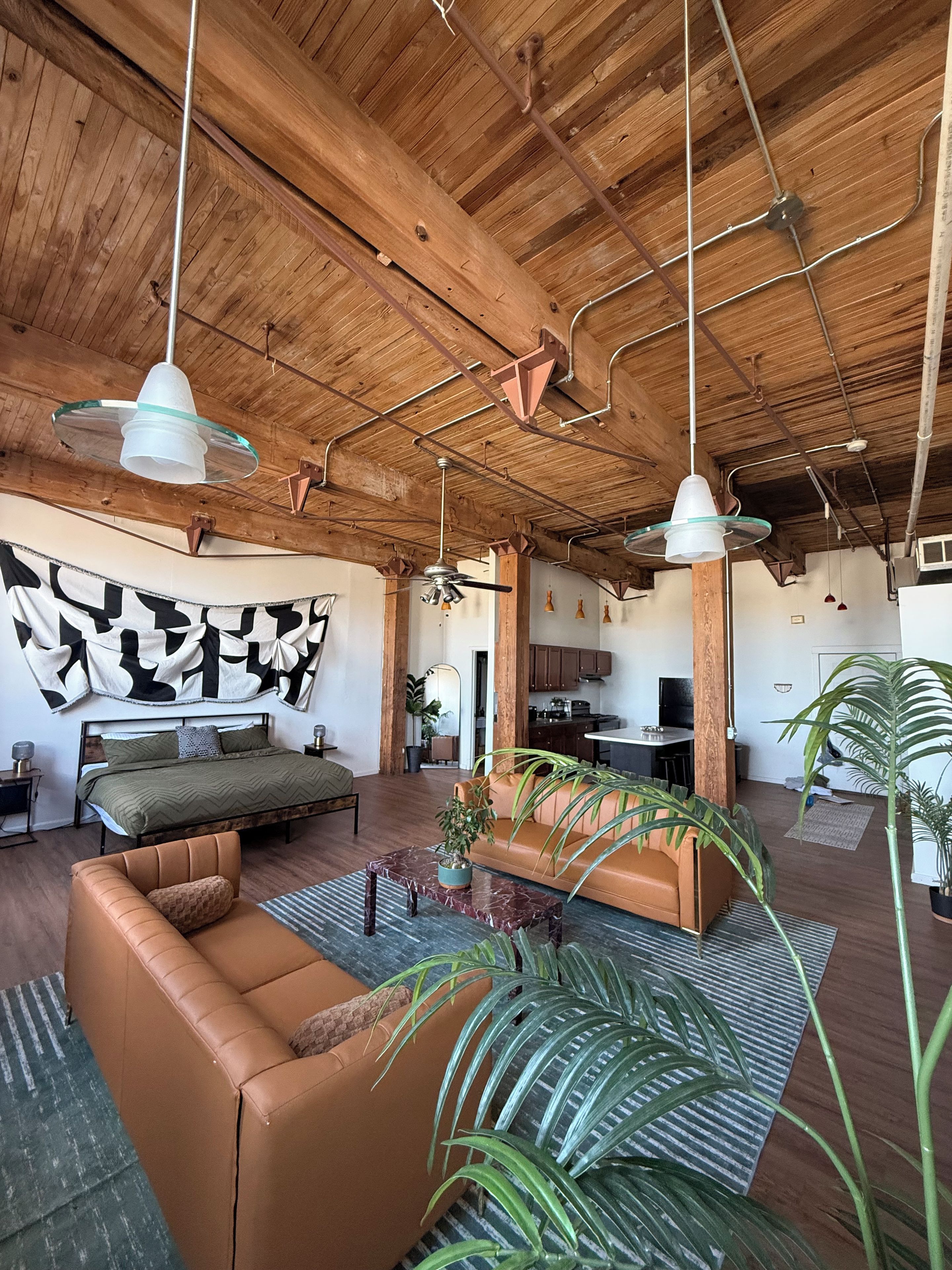 A spacious living area with a high wooden ceiling, a large bed, a sofa, and a dining table.
