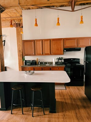 A kitchen with wooden cabinets, a white countertop, a black stove, and two bar stools. - 420-Friendly King suite Loft Walk to Detroit Riverfront FREE parking (Detroit)