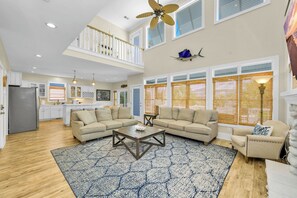 A spacious living room with a high ceiling, a ceiling fan, and a large window with a view. - OIB Waterfront Retreat w/ Dock & Golf Cart 5BR (Ocean Isle Beach)