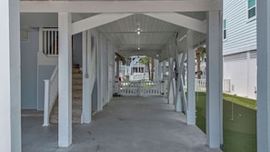 A covered walkway with white pillars, a concrete floor, and a view of a building with a balcony. - OIB Waterfront Retreat w/ Dock & Golf Cart 5BR (Ocean Isle Beach)