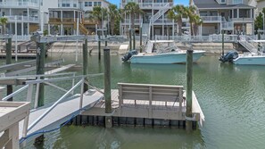 A marina with docked boats, wooden walkways, and a view of residential buildings in the background. - OIB Waterfront Retreat w/ Dock & Golf Cart 5BR (Ocean Isle Beach)