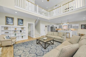 A spacious living area with a high ceiling, a staircase, a kitchen, and a dining area. - OIB Waterfront Retreat w/ Dock & Golf Cart 5BR (Ocean Isle Beach)