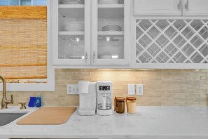 A kitchen with white cabinets, a coffee maker, a jar, and a window with blinds. - OIB Waterfront Retreat w/ Dock & Golf Cart 5BR (Ocean Isle Beach)