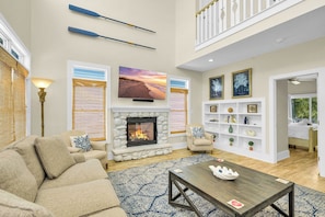 A spacious living room with a fireplace, a sofa, a coffee table, and a television mounted above the fireplace. - OIB Waterfront Retreat w/ Dock & Golf Cart 5BR (Ocean Isle Beach)