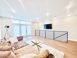 A spacious living room with a large window, a mounted TV, and a modern railing. - Luxurious 3BR @ H St Corridor Free Cancellation (Washington)