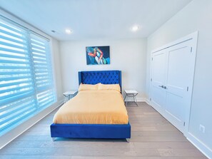 Um quarto com cama, quadro, mesa de cabeceira e guarda-roupa.