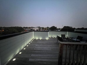 Une terrasse sur le toit avec un plancher en bois, un espace salon avec des chaises et une rambarde.
