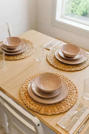 A dining table set with plates, bowls, glasses, and cutlery, with woven placemats and a window in the background. - Charming Farmhouse Near Calgary & Spruce Meadows (East)
