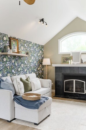A living room with a sofa, a fireplace, a floral wallpaper, and a window. - Charming Farmhouse Near Calgary & Spruce Meadows (East)