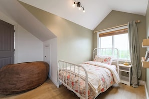 A bedroom with a bed, a wooden bench, a window with curtains, and a ceiling light fixture. - Charming Farmhouse Near Calgary & Spruce Meadows (East)