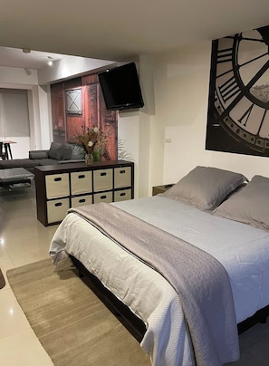 A modern bedroom with a bed, a dresser, a flat-screen TV mounted on the wall, and a large clock. - Depto 203 (Ciudad de México)