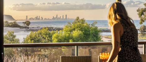 A woman seated at a table with a view of a coastal cityscape.