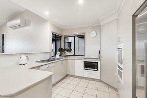 A modern kitchen with white cabinetry, a built-in oven, and a microwave. - Currumbin Beachside Retreat (Currumbin)