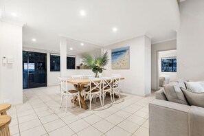 A modern living room with a dining area, a large window, and a view of the beach. - Currumbin Beachside Retreat (Currumbin)