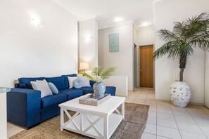 Un saló amb un sofà blau, una taula de centre blanca i una planta en test.
