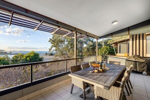A balcony with a wooden table, wicker chairs, and a view of the sea and trees. - Currumbin Beachside Retreat (Currumbin)