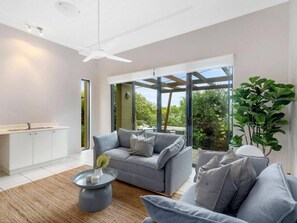 Ein modernes Wohnzimmer mit einem grauen Sofa, einem Couchtisch und einem großen Fenster mit Blick auf Grünflächen.